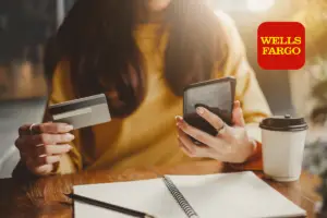 Picture of a woman holding her Well Forgo Credit card in one hand and her phone in te other.