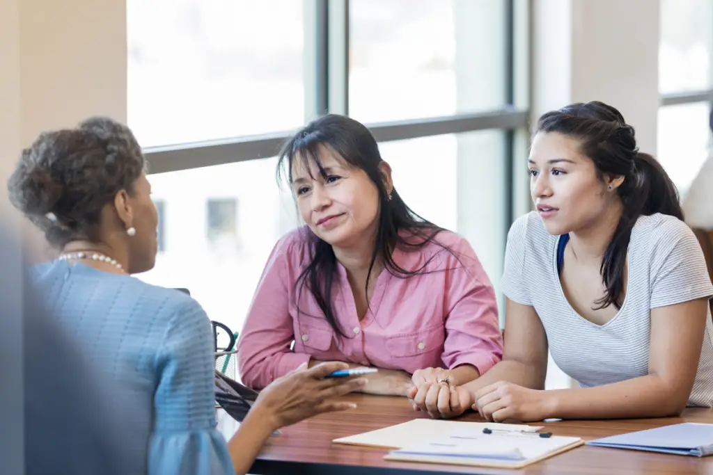 Three people researching loan options on a laptop with tuition bills and credit reports spread out on a desk