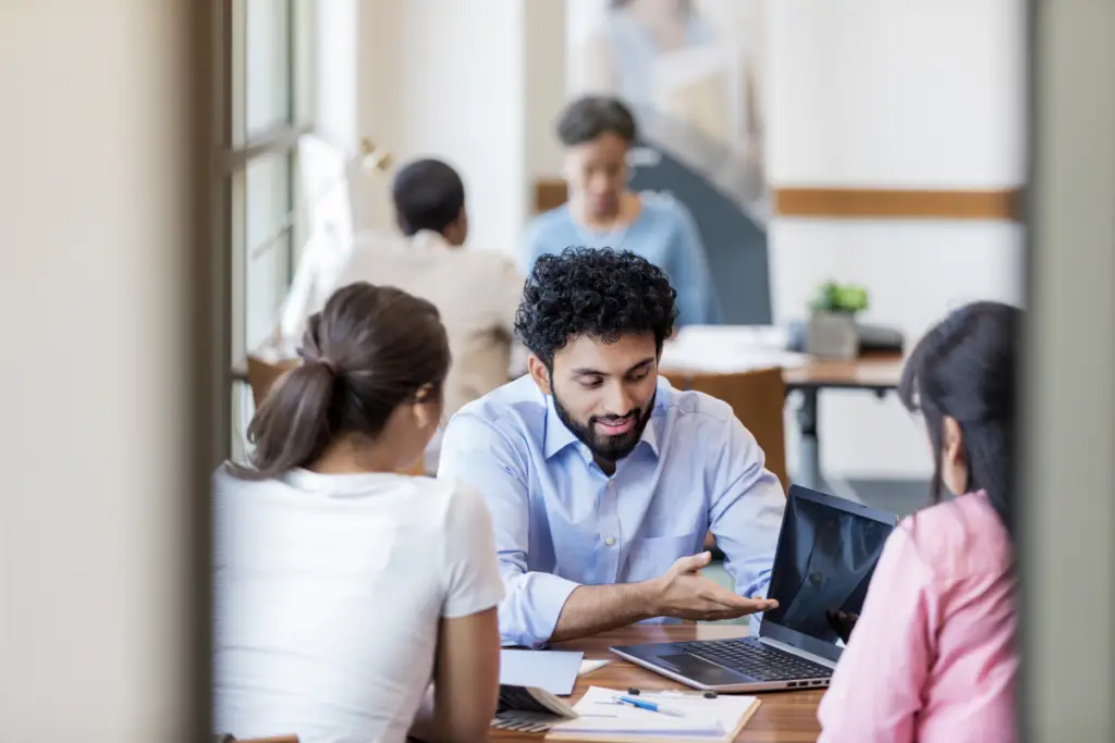 Three people sitting at a desk, surrounded by paperwork and a laptop, looking stressed while trying to navigate the application process for an 8k personal loan for tuition with bad credit